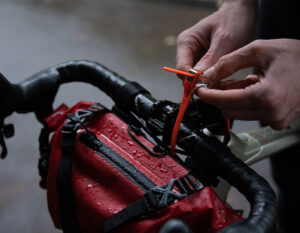 man securing a saddle bag to the handlebars of a wet bicycle