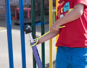 child locking a scooter to a colourful fence in a playground with a z lok