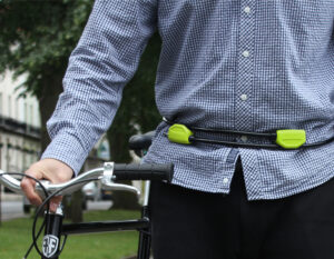 man pushing along a bicycle through a park with a wearble hiplok pop bike lock around his waist