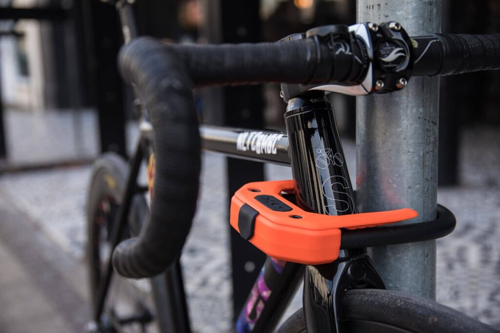 Hiplok DX orange locking headtube of fixed gear bike in a urban area around the head tube and a lamp post