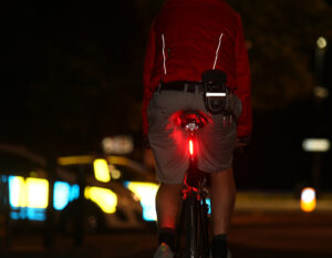 man riding road bike at night with a d lock clipped to belt with reflective strips